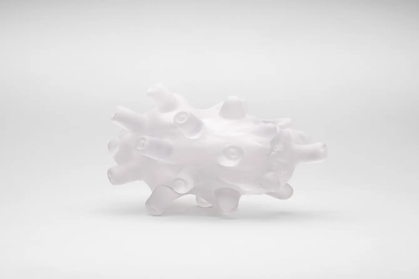 サンドブラスト加工（砂を吹きつけて曇りガラス状にする技法）が施されている吸盤のようなパーツが集まったガラス製の作品が白い床の上に置かれている。表面の質感は光沢が少しあるがきめ細かい凹凸がある。吸盤のようなパーツは全て異なる方向を向いているが、位置が均等に配置されている。３つの吸盤のようなパーツが作品全体を支えている。