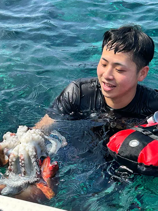 野田紘がダイビングをしている様子を写した写真。海中に入って片手にタコをもち、タコの様子を眺めている。